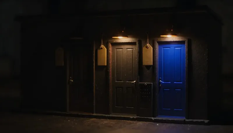 Miniature night diorama: three model front doors in one wall beside a key board, the middle handle glowing cobalt.