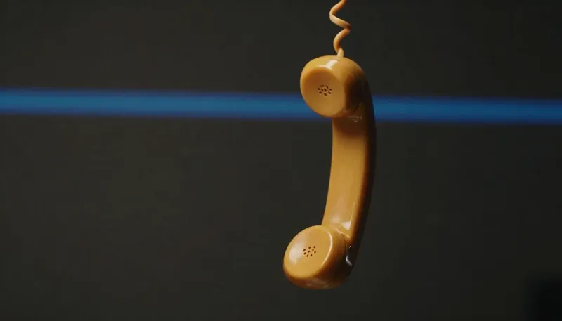 Miniature night diorama: close-up of a wall phone with its amber handset swinging off the hook, missed-call lamps glowing along a cobalt strip beneath